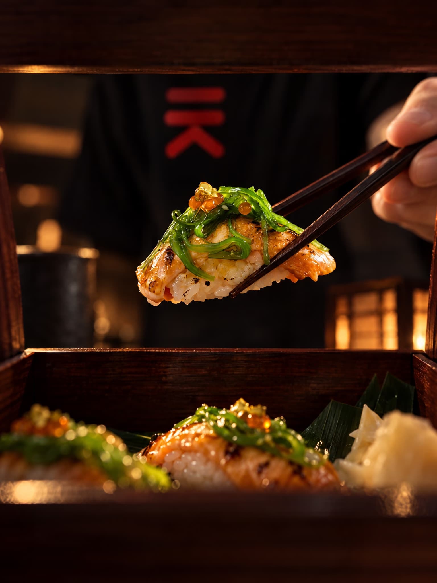 Unos palillos levantan un nigiri de salmón flambeado con alga wakame y huevas